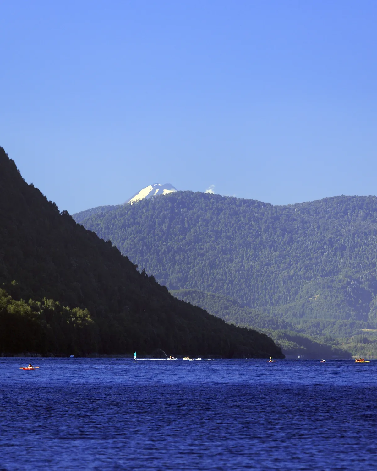 Lago Caburgua with forested hills and a snow peak