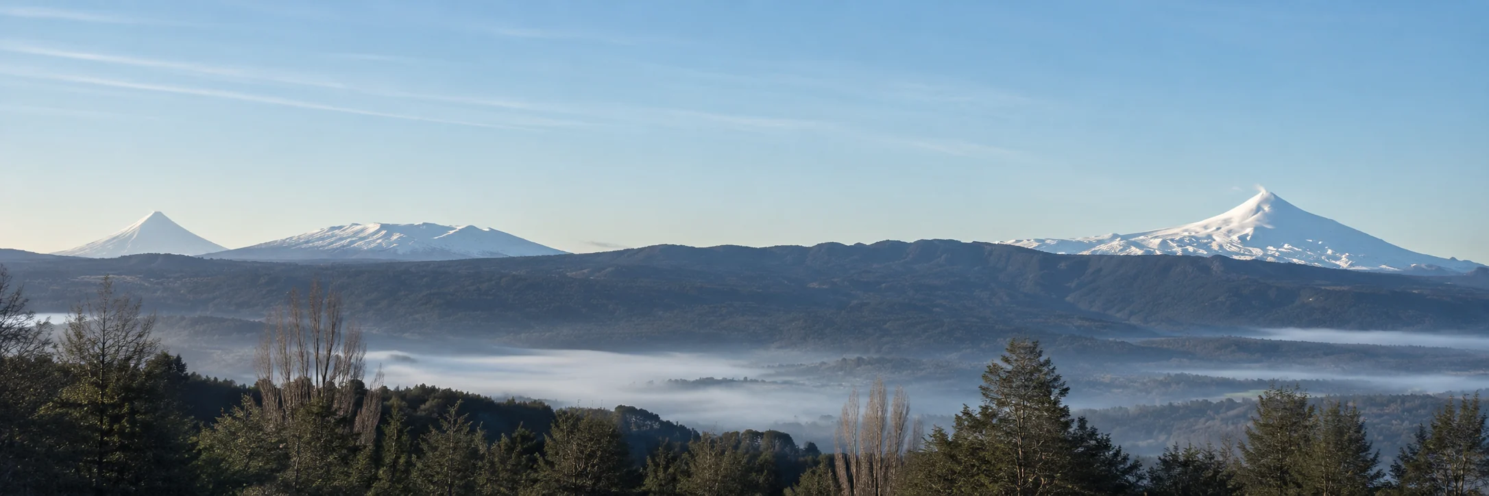Panorama from the upper row looking south to south-west: Lanín and Quetrupillán on the left, a long forested ridge, Villarrica on the right, fog in the valley